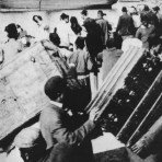 Fotografia histórica em preto e branco de uma multidão em desembarque, com pessoas apoiadas na amurada